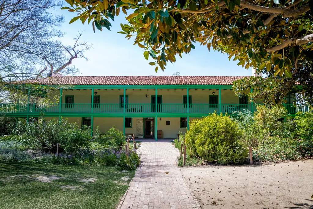 Historic two-story adobe house with garden view.