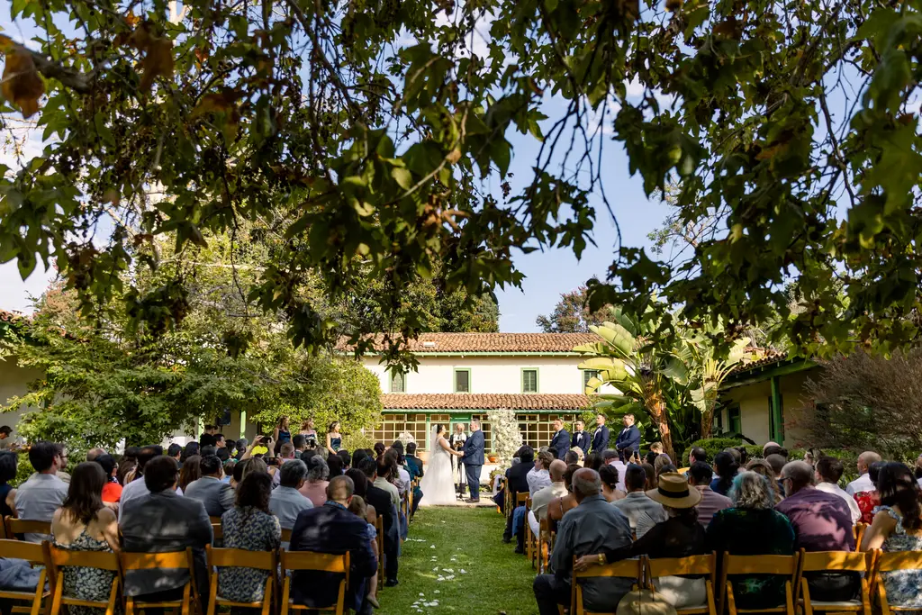 Outdoor wedding ceremony under leafy trees.
