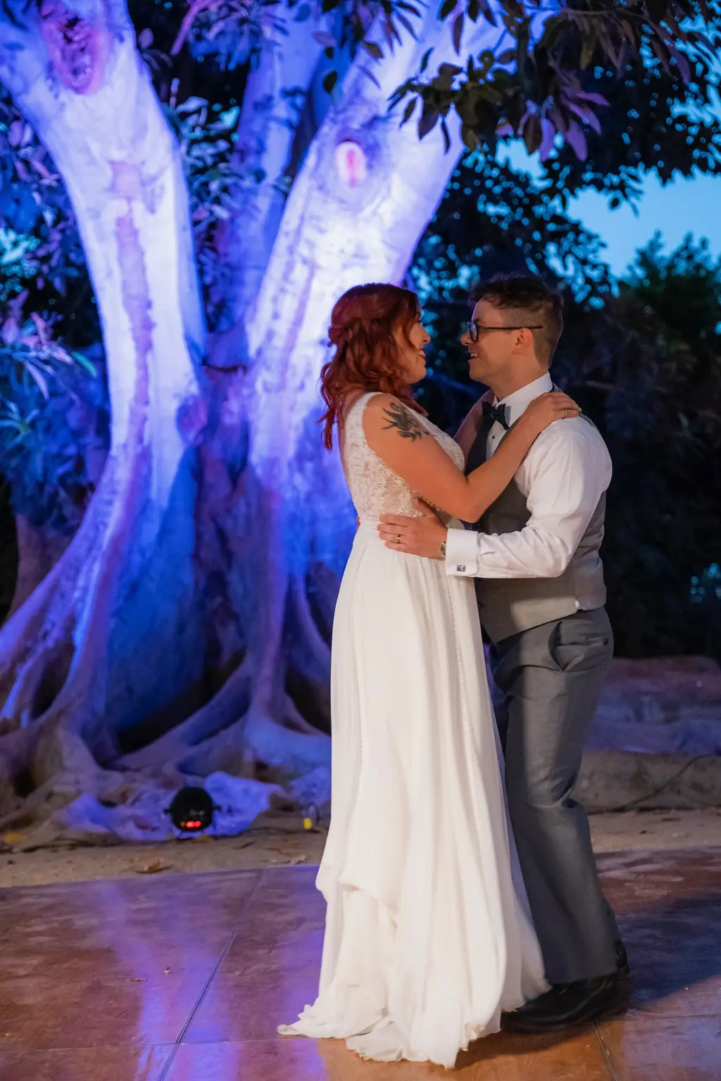 Couple dancing in front of illuminated tree at night.