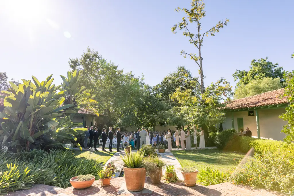 Outdoor wedding ceremony with attendees and greenery.