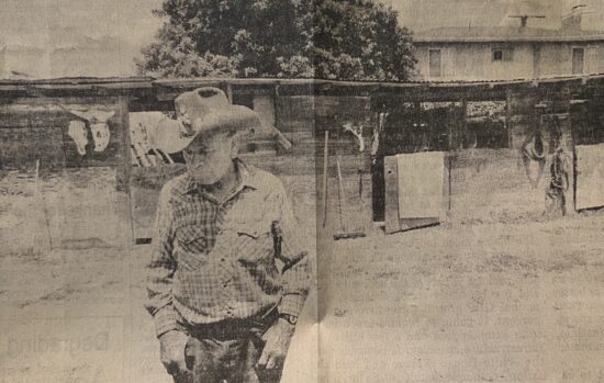 Man in cowboy hat near rustic barn.