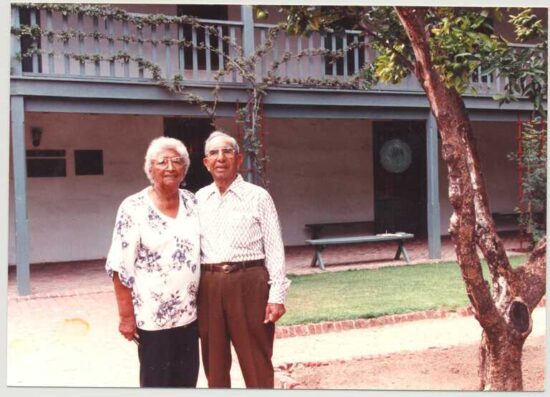 Elderly couple standing by tree outside building.